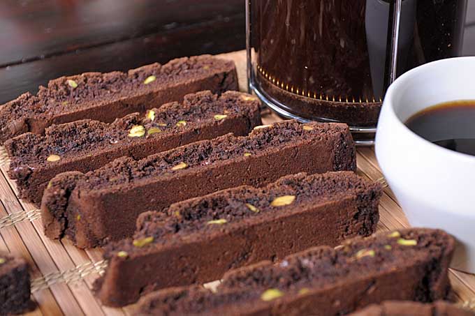 Close up of rows of chocolate pistachio biscotti with a white coffee cup | Foodal