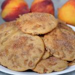 Close up of a plate full of peach cookies. 3 pieces of fresh fruit is in the background | Foodal