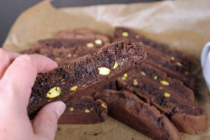 Human fingers reaching for a chocolate pistachio biscotti cookie | Foodal