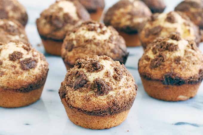 Twelve streusel-topped muffins on a gray and white marble surface.