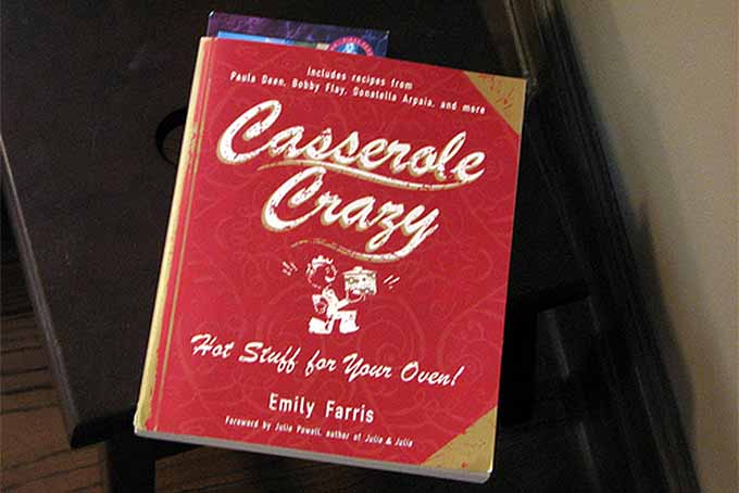 Book with red cover called Casserole Crazy, on a brown table.
