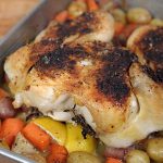 A roasted lemon chicken carcass over a bed of potatoes and carrots inside of a cake pan showcasing a crispy skin | Foodal