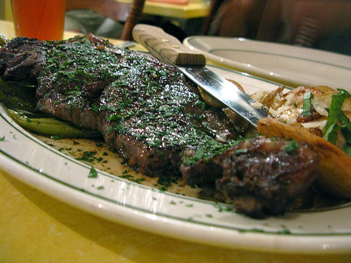 A close up view of a flavorful steak with a knife resting on top.