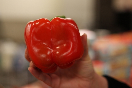 A hand holding a single red bell pepper.