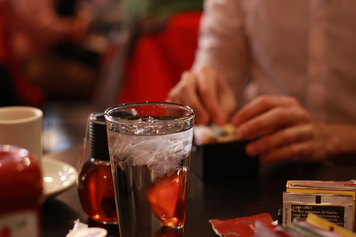 An image of tall glass of tea on a table with a woman at the back.