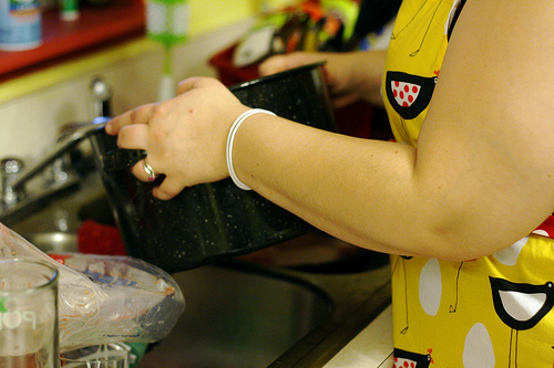 An image of a woman holding a pot over the kitchen sink.