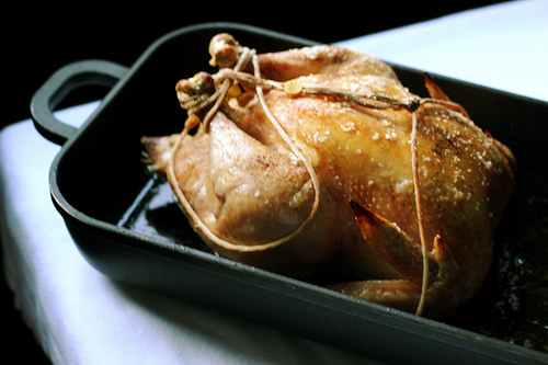 An image of a juicy looking delicious roasted chicken in a black pan. 
