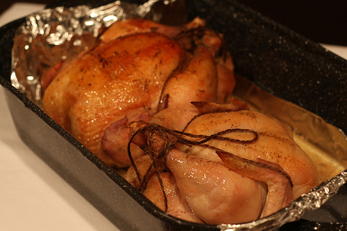 Still warm from the oven, two golden brown roasted chicken in a baking pan lined with foil. 