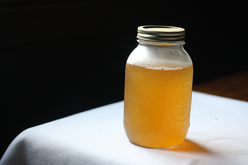 An image of a glass jar, filled with kombucha, on top of a table.