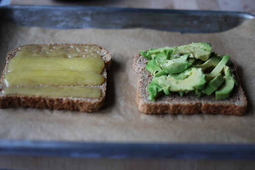 An image of two pieces of bread with one covered with mashed avocado and the other with thin slices of cheese.