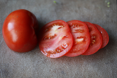 An image of a ripe tomato, one whole a few slices beside it.