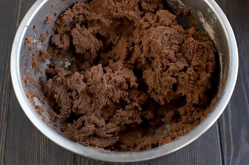 Chocolate cookie dough in a stainless steel bowl, on a dark brown wood background.