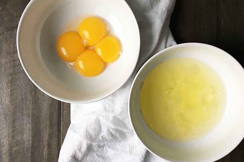 Horizontal image of separated egg yolks and whites in two white bowls.
