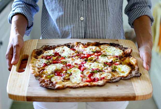 A man carries a wooden cutting board loaded with a Strawberry Leek Pizza with Kefir-Soaked Einkorn Crust.