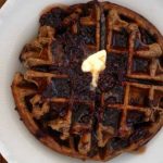 Top down view of a Chocolate Chip Einkorn Belgian Waffle on a white ceramic plate.