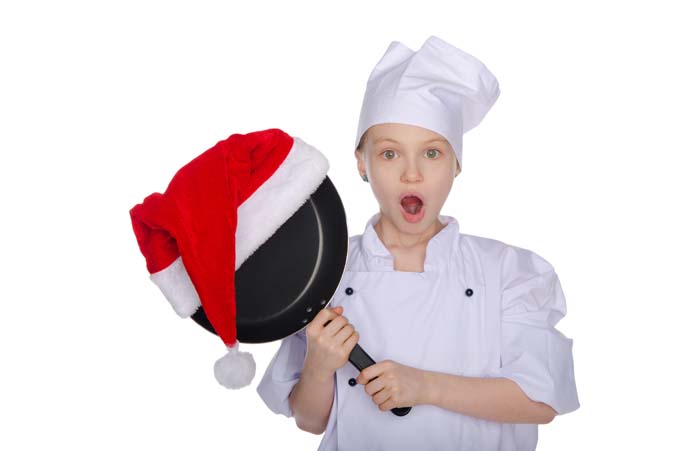 Young chef holding a nonstick frying pan topped with a Santa hat, isolated on a white background.