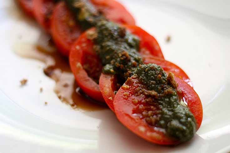 Vegan Basil Walnut Pesto spread up top a row of sliced tomatoes.