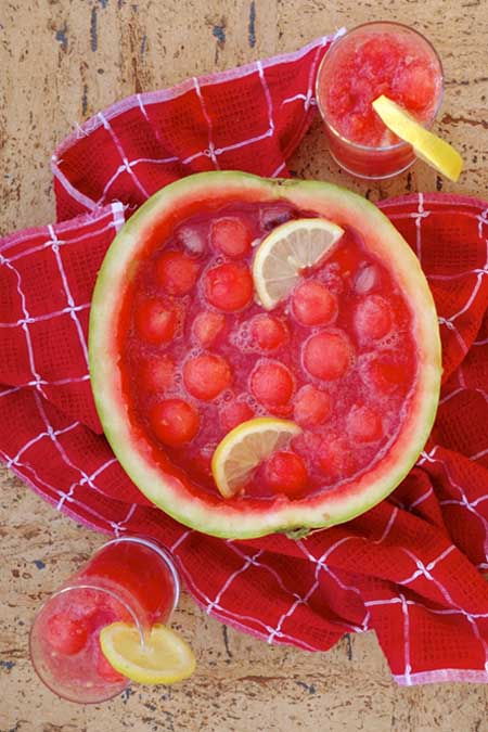 Overhead image of Watermelon Bowle Punch served in a hollowed-out melon and garnished with lemon slices.