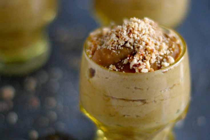 Close up of a an individual portion of a Stovetop Squash Pudding with Toasted Hazelnuts recipe in a clear glass serving container.