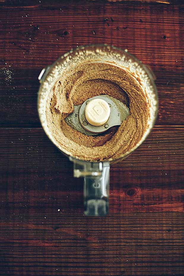 Overhead view of a food process full of soaked vanilla maple almond butter on a dark wooden background.