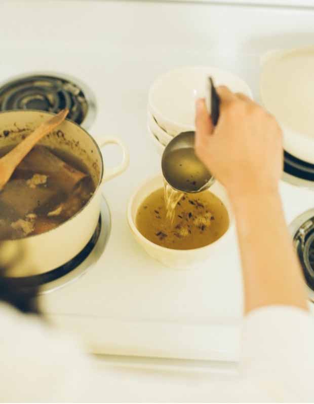 The author uses a ladle to dip some perpetual beef bone broth from a stockpot to a small bowl.