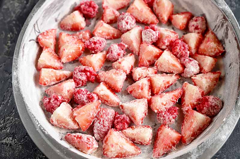 Horizontal image of sliced strawberries and raspberries covered in a light dusting of flour in a pan.