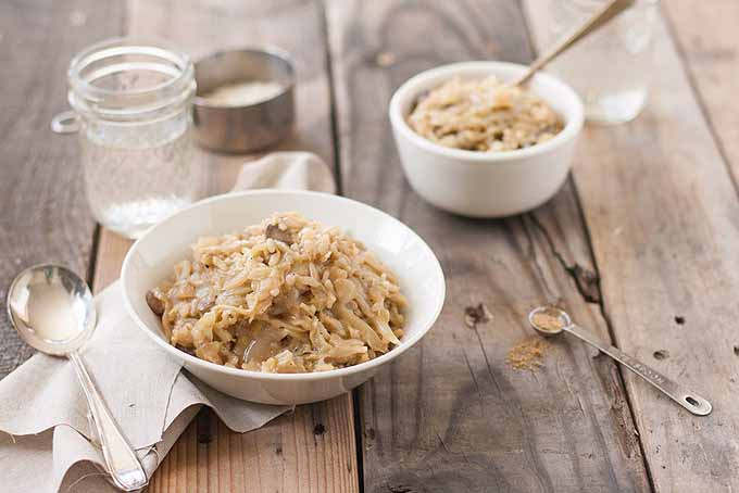 Oblique photo of two bowls of cabbage mushroom risotto on a rustic, wooden table top.