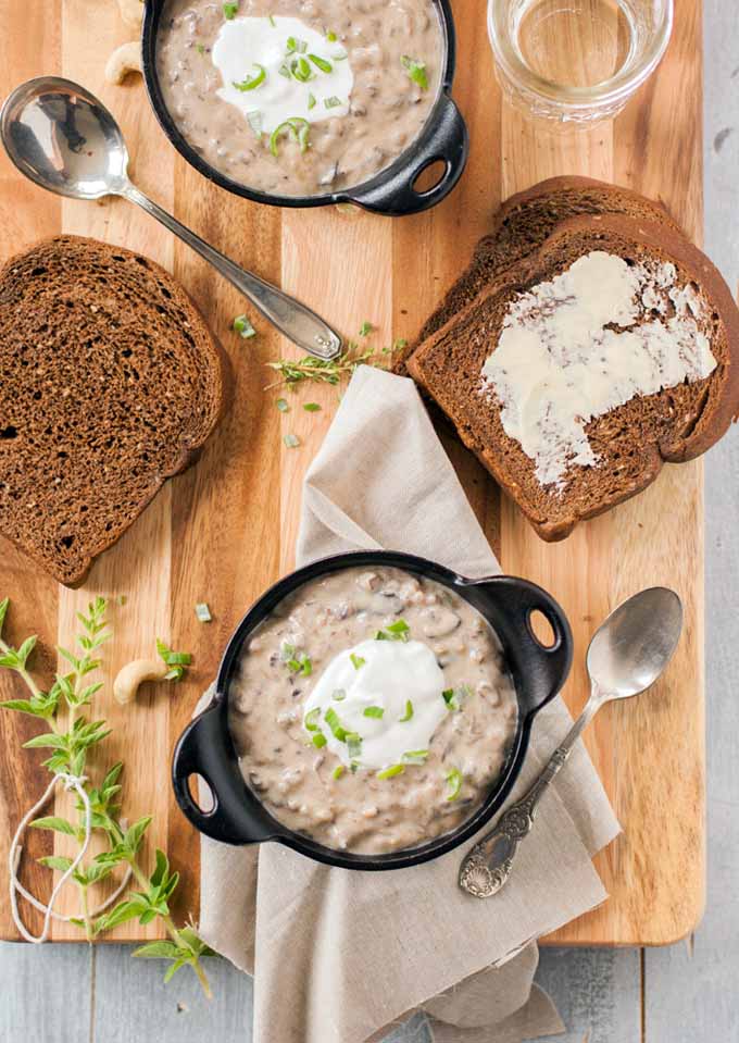 Top down view of two bowls of vegan cashew cream wild rice and mushroom soup with two slices of brown bread on a large maple cutting board.