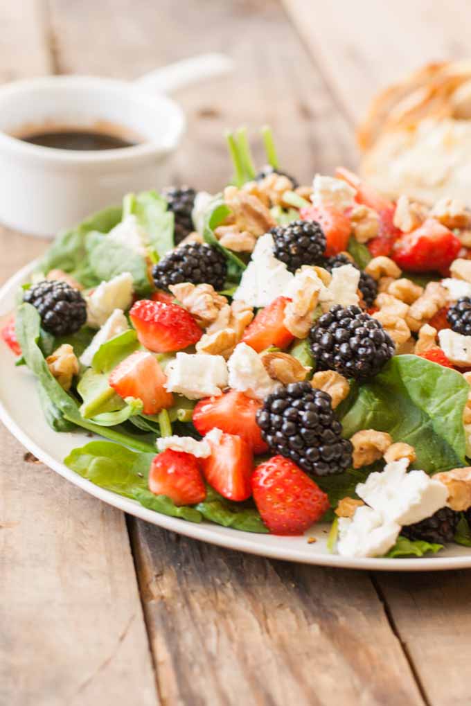 A close up of a fresh berries and spinach salad recipe showing half a plate full on a rustic wooden background.