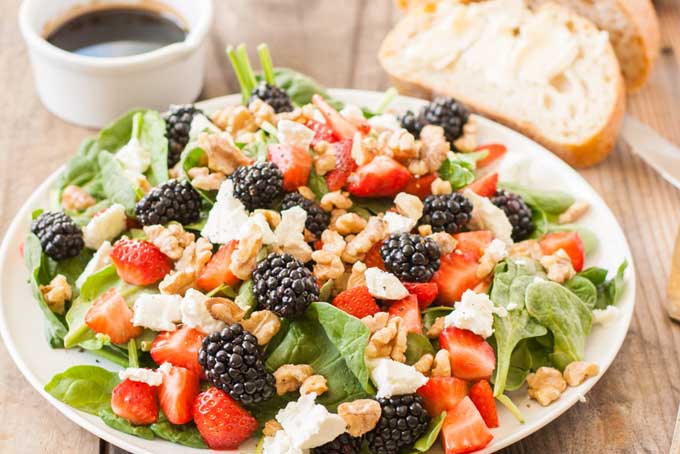 A fresh berry and spinach salad on a porcelain plate which is sitting on a rustic wooden table.