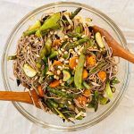 Top down view of a clear glass mixing bowl full of grilled veggie soba salad.