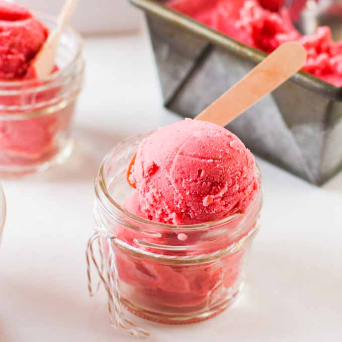 A close up of a clear glass serving dish filled with strawberry goat cheese sherbet.