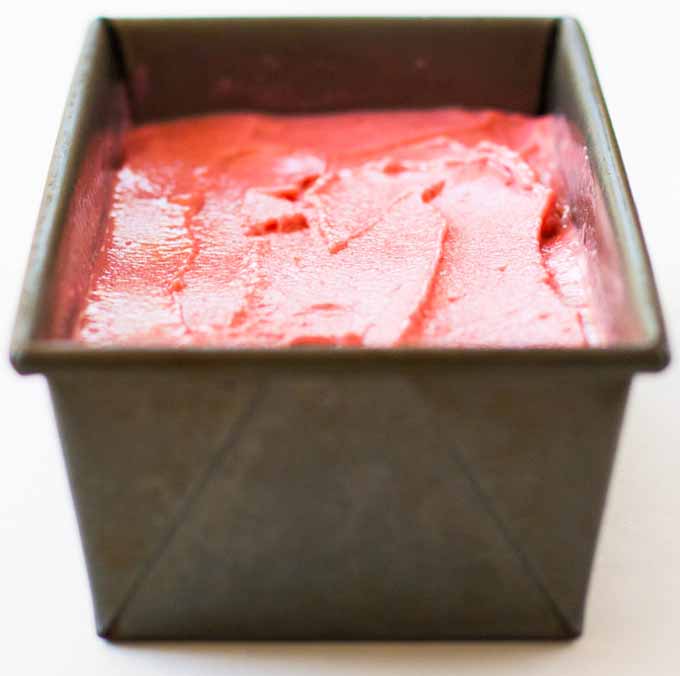 A metal tub full of frozen strawberry goat cheese sherbet on a white, isolated background.