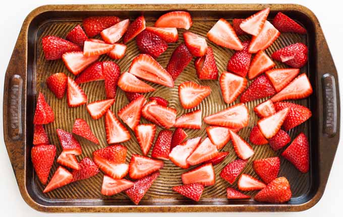 Top down view of a metal baking tray full of chopped fresh strawberries.
