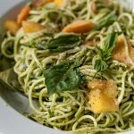 Close up of a white, porcelain bowl full of Zucchini Spaghetti with Peaches and Pumpkin Seed Pesto.