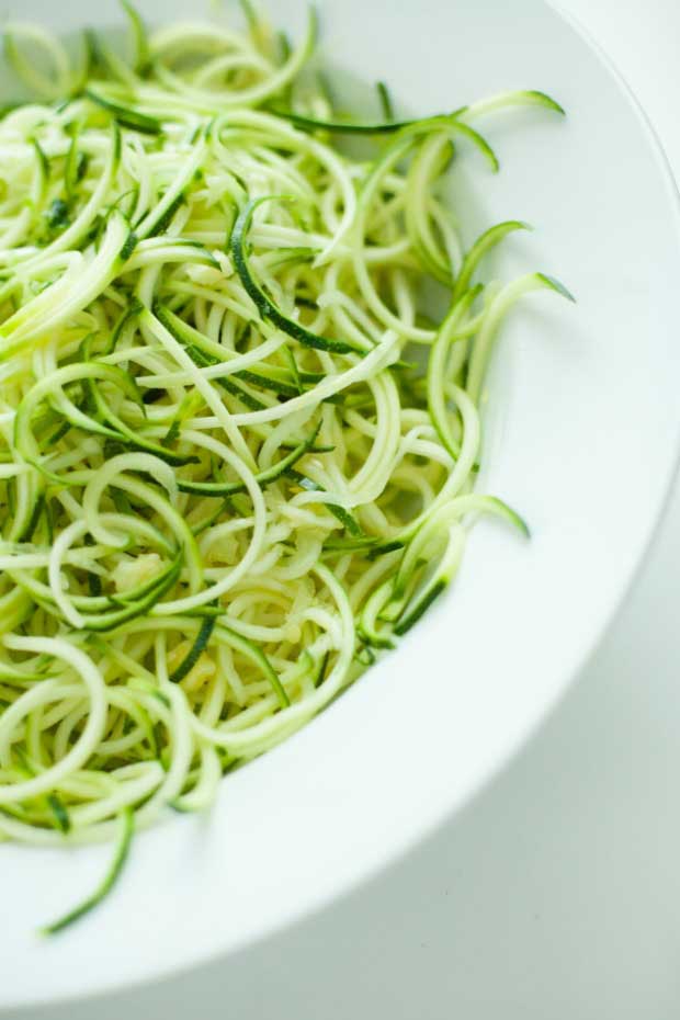 Close up of raw zucchini noodles or zoodles in a white, porcelain bowl.