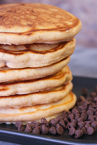 A stack of Cinnamon Chocolate Chip Pancakes with extra chocolate chips spread on the side.