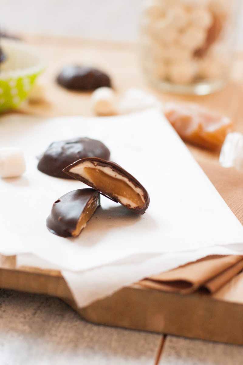 Close up of a chocolate covered marshmallow covered caramel that has been split in half to show the insides.