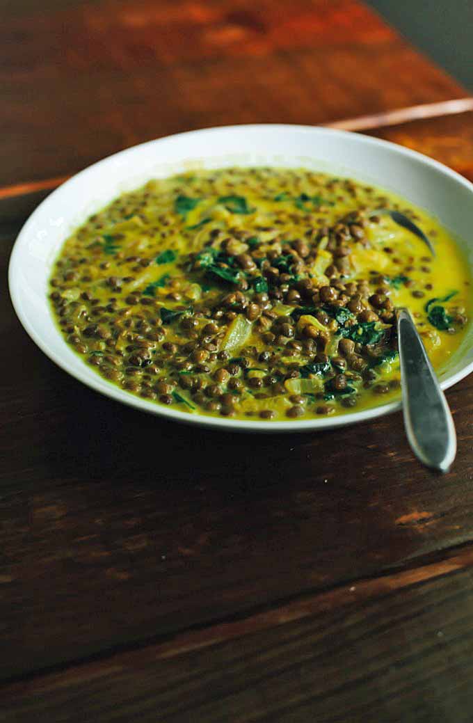 A white porcelain bowl filled with a French lentil soup made with chard and spiced with turmeric.
