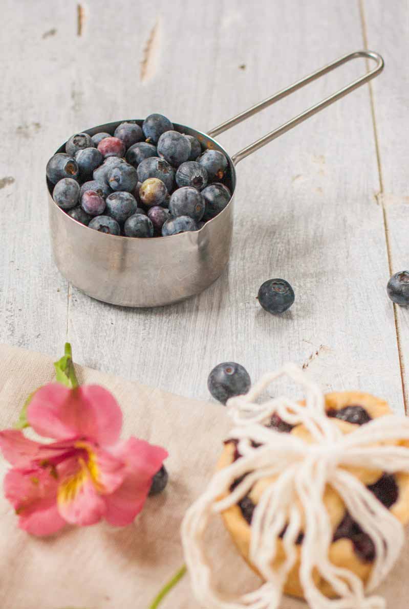 A measuring cup full of fresh blueberries on a white rustic wooden table top.