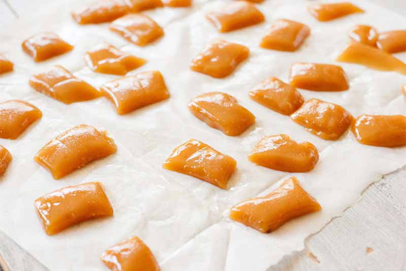 Flat, rectangular homemade caramel candy portioned into small pieces on a piece of waxed paper.