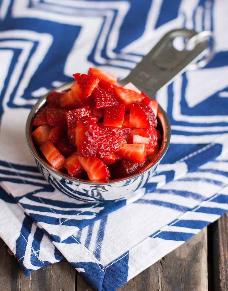 Oblique view of a stainless steel measuring cup full of chopped fresh strawberries.