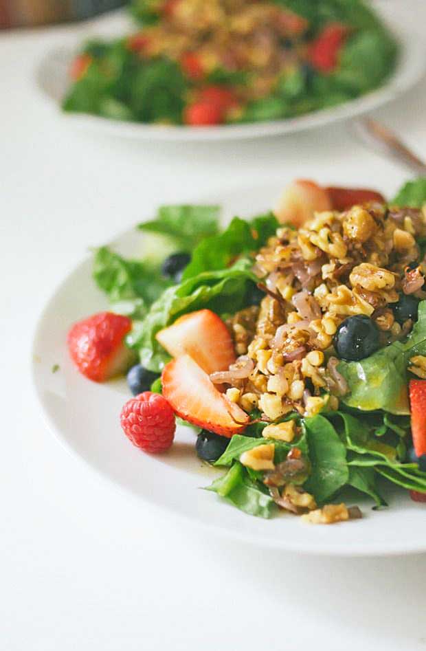A closeup of a half plate full of triple berry salad that includes leaf lettuce, shallots, and walnuts.