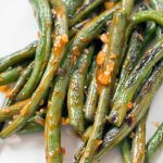 Closeup of sauteed green beans with hot sauce and minced garlic, on a white plate.