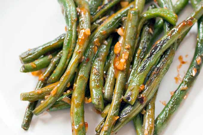 Closeup of sauteed green beans with hot sauce and minced garlic, on a white plate.