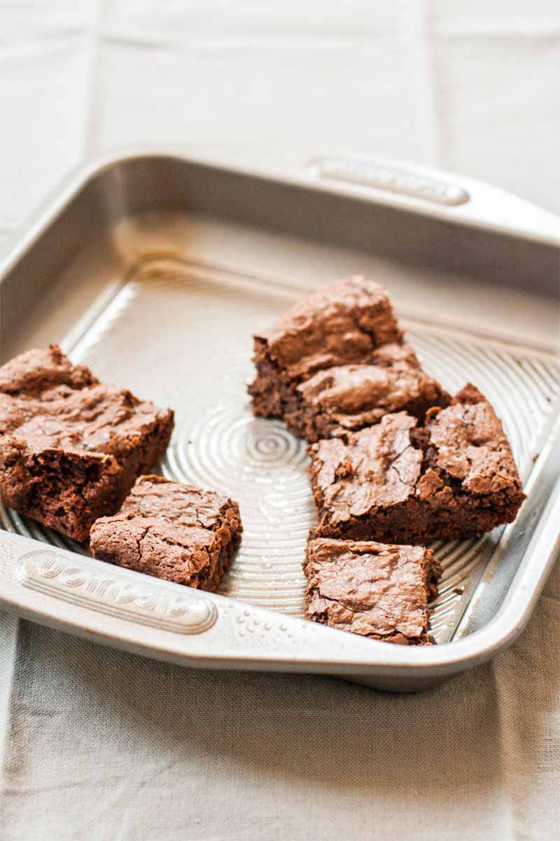 Five brownies in a metal baking pan, on a table topped with a wrinkled gray cloth.