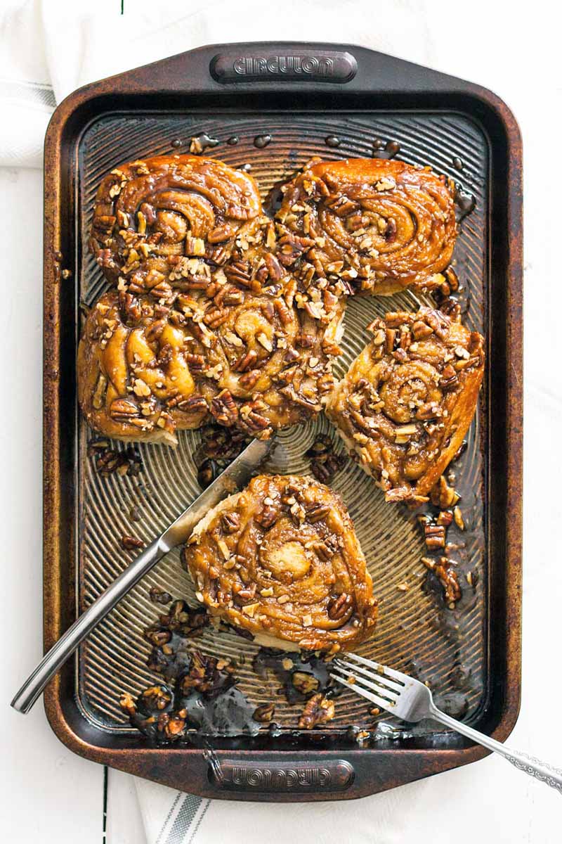 Top-down shot of a brown metal baking sheet with pecan sticky buns and two forks, on a white background.