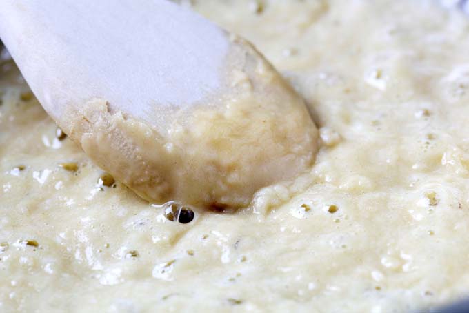 Extreme closeup of béchamel sauce, being stirred with a wooden spoon.