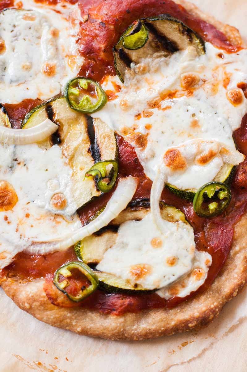 A closeup and overhead shot of the gooey melted mozzarella cheese on top of a grilled zucchini pizza. 