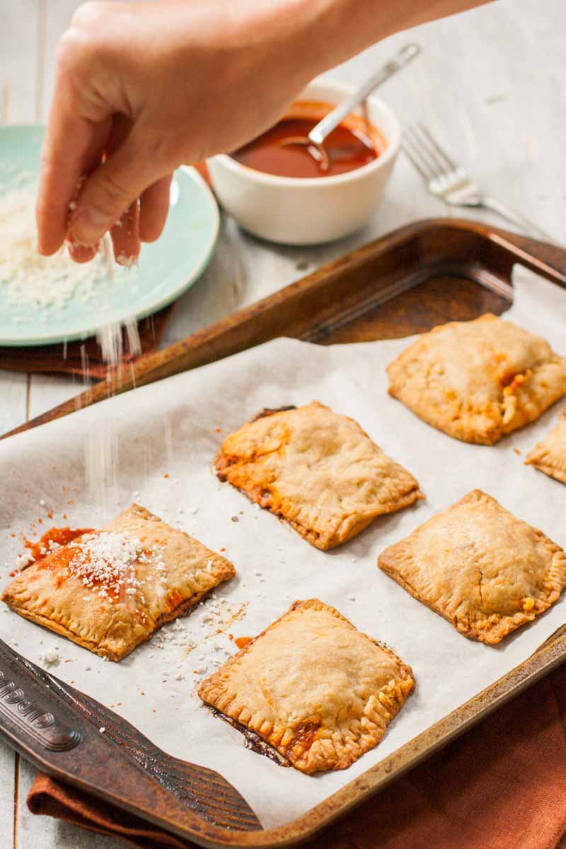 A human hand sprinkles grated Mexican cotija cheese over the top of homemade empanadas.